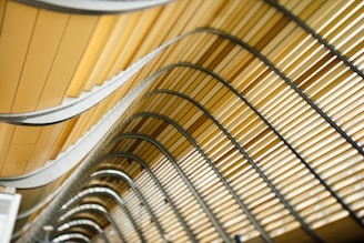 Curved architectural design featuring a series of parallel, wavy lines and metallic structures in shades of yellow and beige.