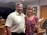 A smiling real estate agent showing a property to a couple in a bright living room.