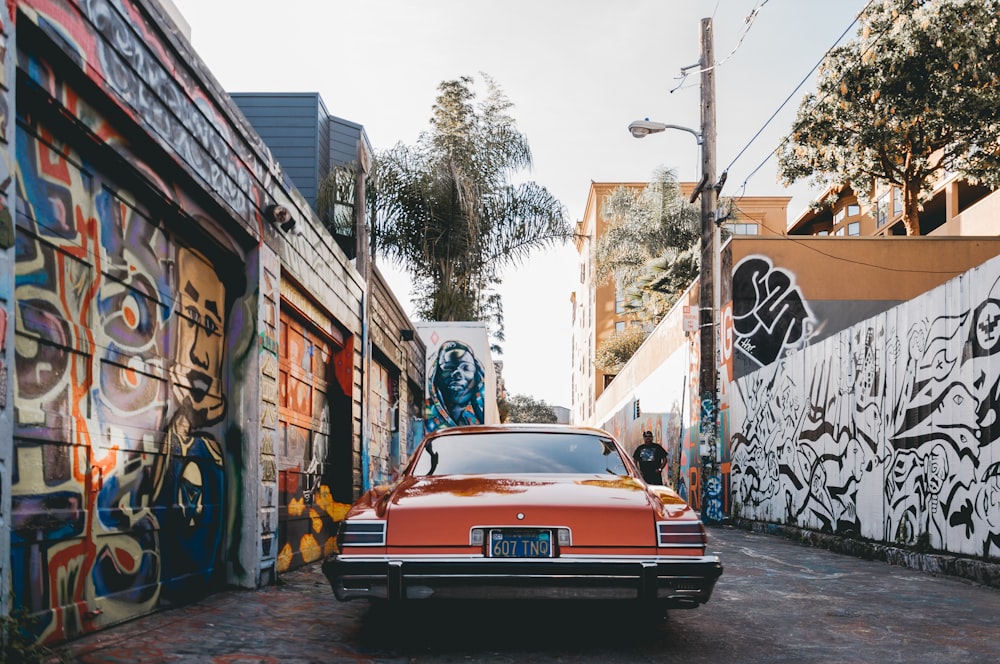 Voiture orange garée entre les murs peints