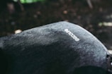 A close-up view of a fabric surface of a backpack with the brand name 'Incase' visible on it. The texture of the material is detailed, showing a rugged or denim-like appearance. The lighting creates shadows and highlights, adding depth to the image.