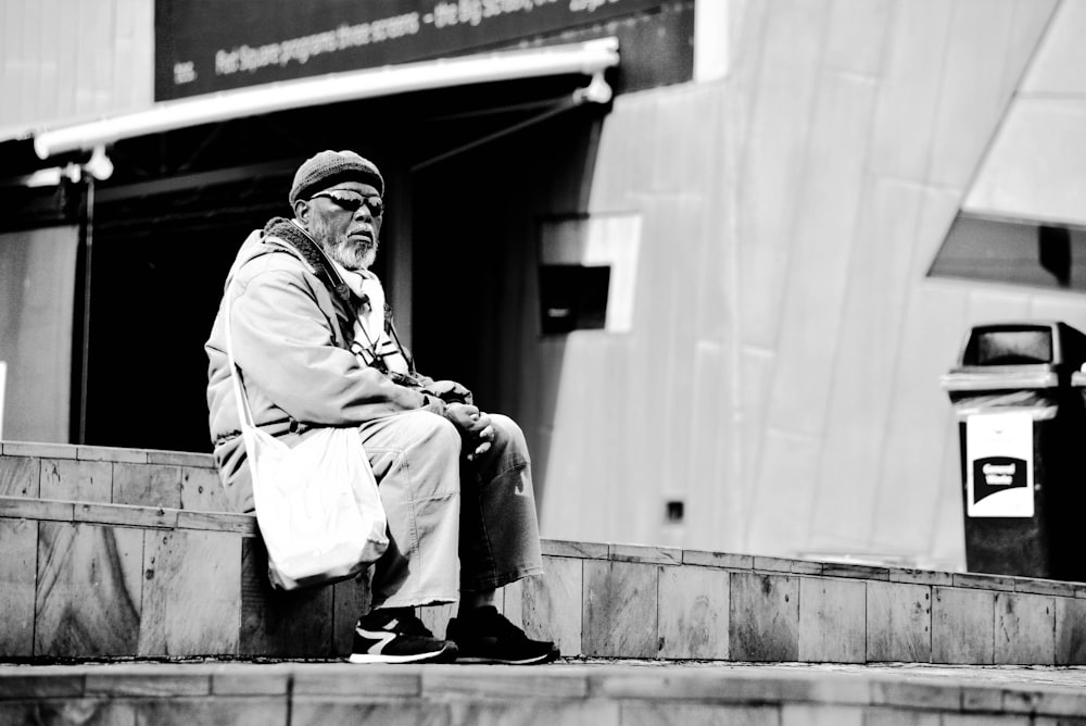 greyscale photograpy of man sitting on gray stair