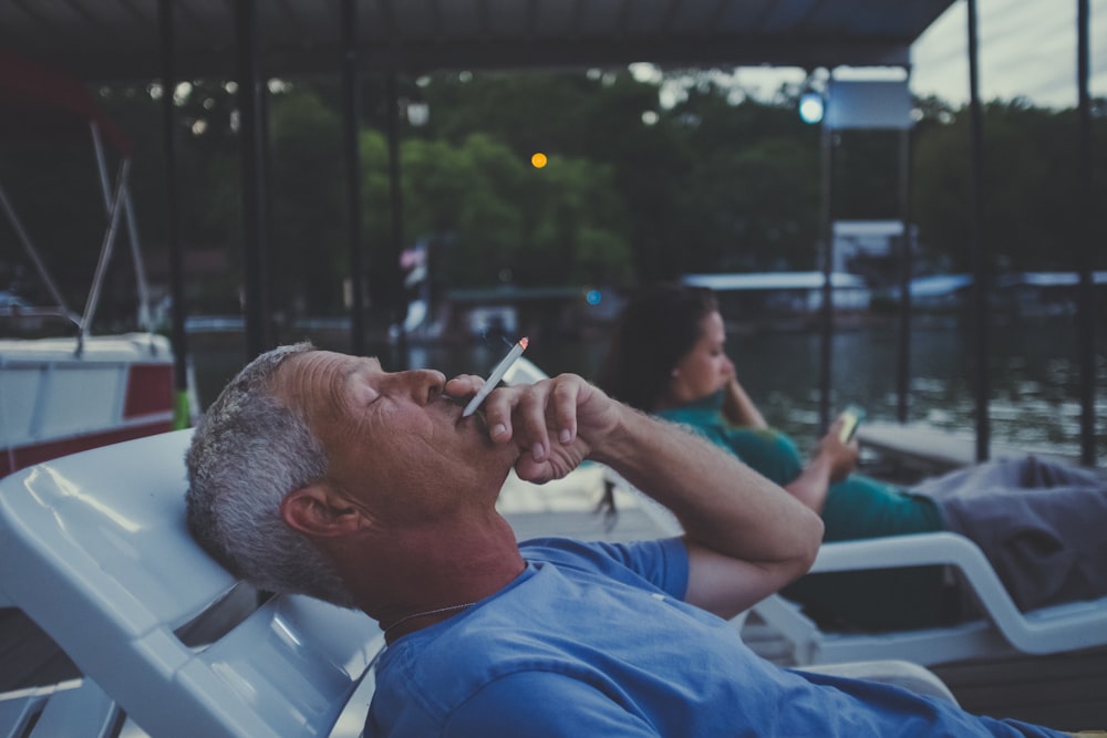 man lying on lounger while smoking cigarette