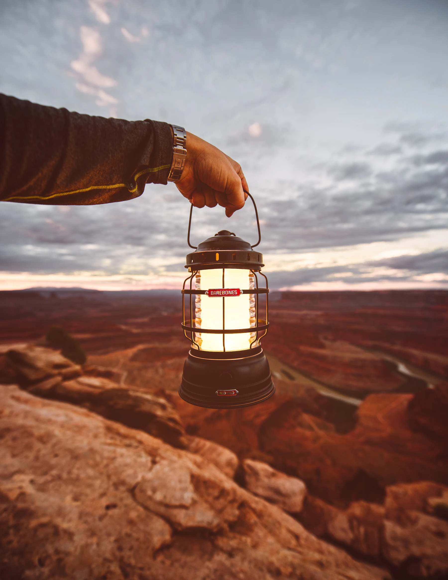 Person holding a portable camping lantern outdoors near sunset
