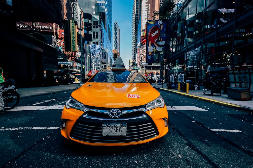 orange Toyota car on road between buildings