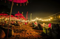Red umbrellas and warm lantern light along a quiet Bali shoreline at night