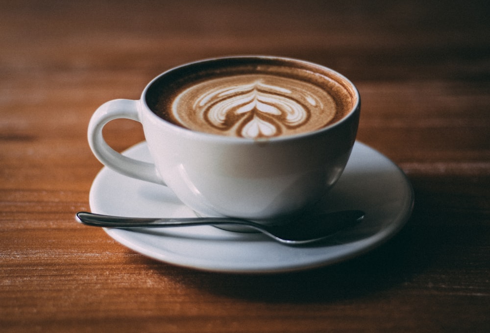 Cappuccino in a white cup on a saucer with foam art and a small spoon