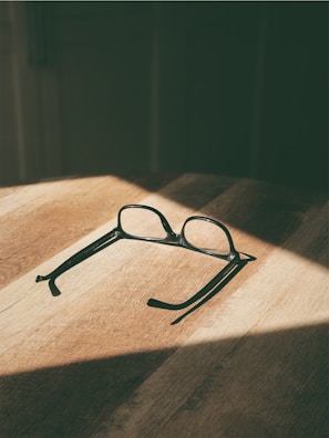 Close-up of trendy grey eyeglasses sitting on a wooden surface with sunlight.