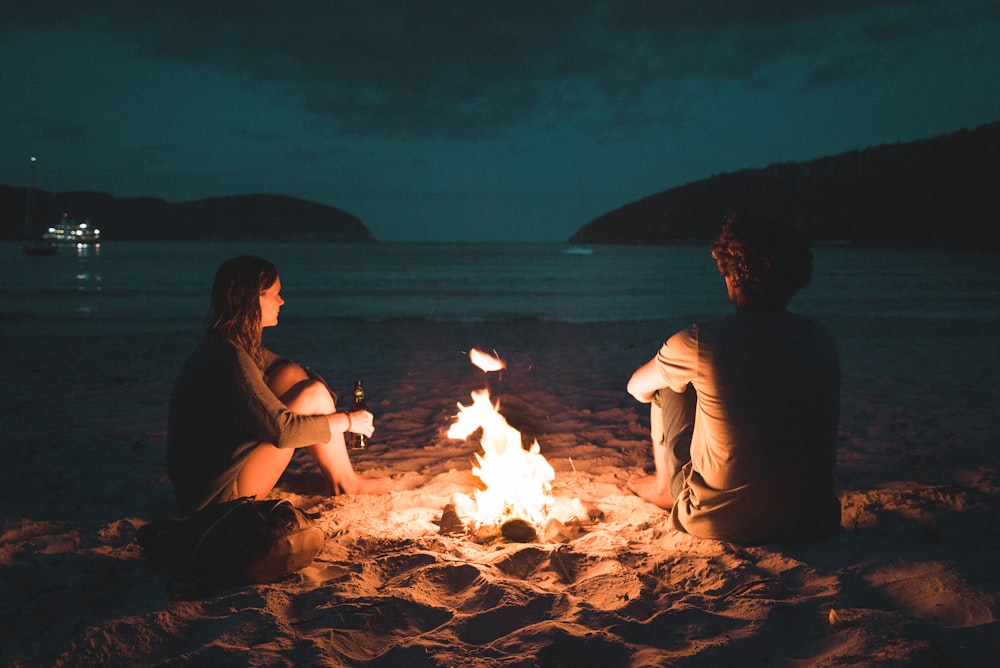 man and woman with bone fire sitting on seashore