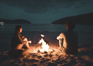 man and woman with bone fire sitting on seashore