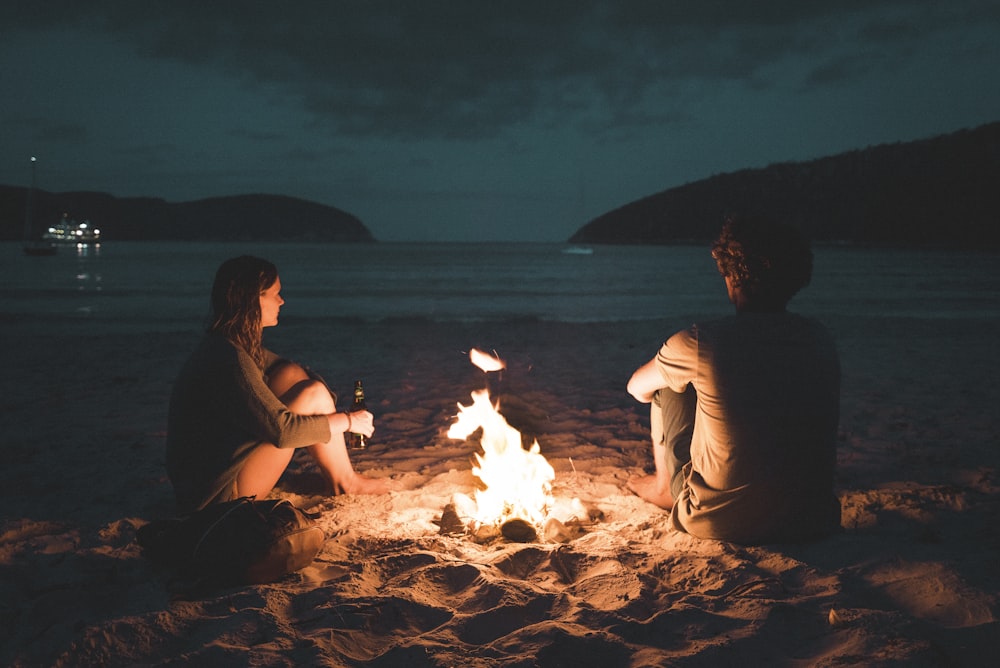 man and woman with bone fire sitting on seashore