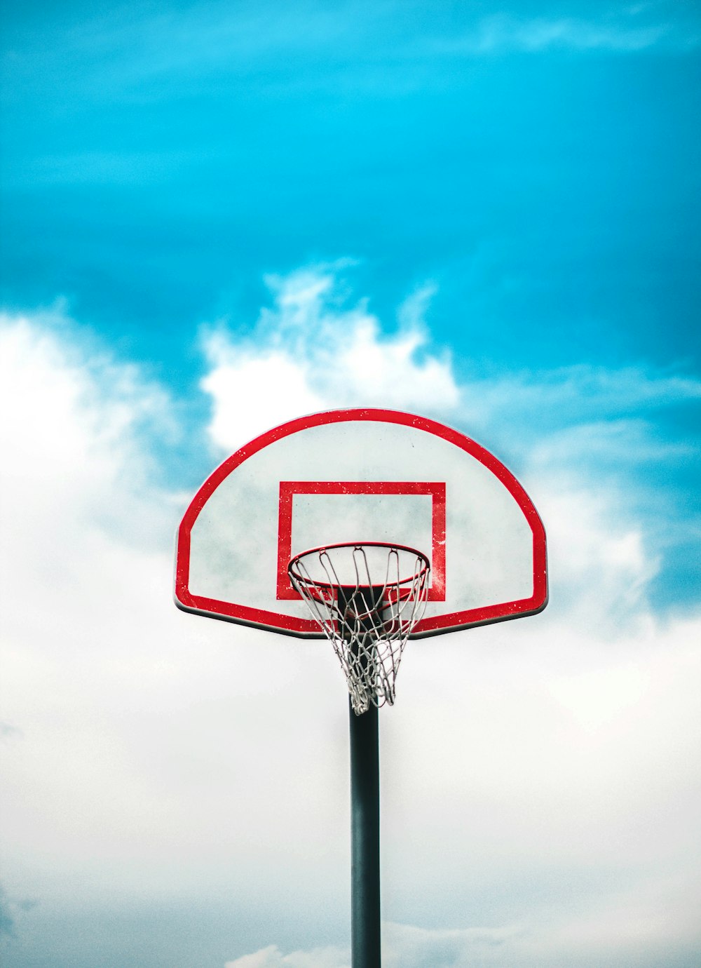 Roter und schwarzer Basketballkorb unter bewölktem Himmel