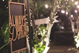 A warmly lit sign with the words 'Always dare to dream' hangs among lush greenery and twinkling fairy lights, evoking a cozy and inviting atmosphere.