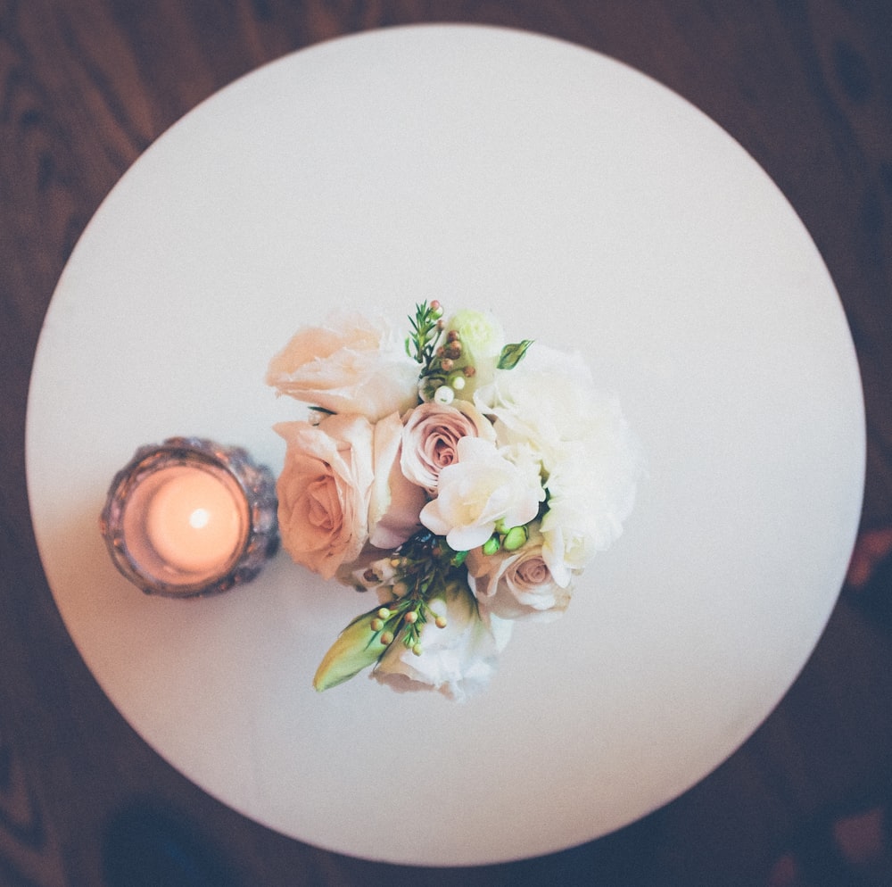 white rose flowers beside lighted candle on round white plate