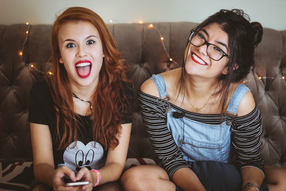 woman laughing beside woman smiling sitting on tufted sofa inside the room