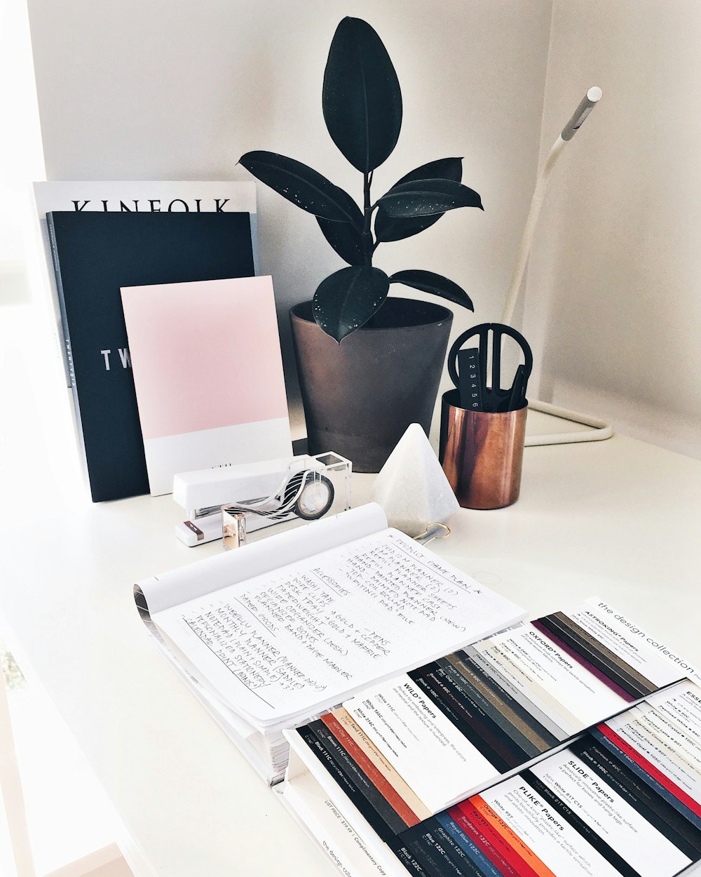 A pile of work books on a white desk.