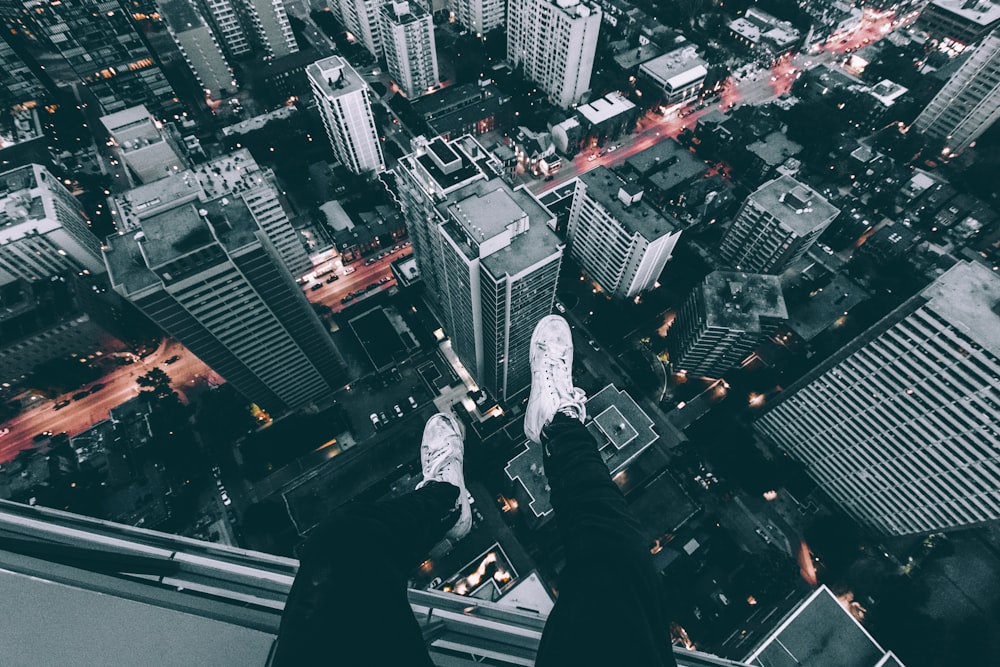 fotografia aerea dell'uomo seduto in cima all'edificio con vista di edifici a molti piani durante il giorno