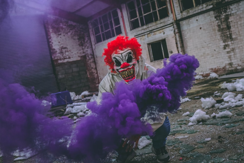 clown holding purple smoke bomb in ruined building