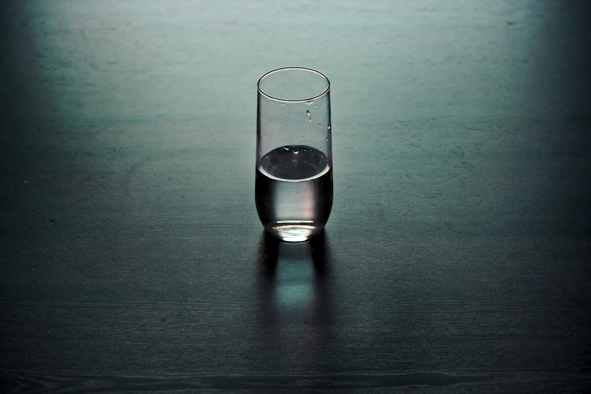 Ein halb volles Wasserglas auf einem dunklen Holztisch im gedämpften Licht