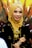 A woman is wearing a golden hijab adorned with an elegant tiara and intricate jewelry. Her attire features gold embellishments that complement the detailed accessories, and she is smiling warmly.