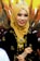 A woman is wearing a golden hijab adorned with an elegant tiara and intricate jewelry. Her attire features gold embellishments that complement the detailed accessories, and she is smiling warmly.