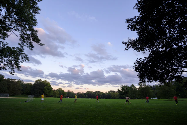 A lively group of fathers playing soccer on a bright green grass field under a clear sky.