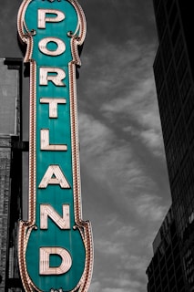 A teal blue Portland sign with a dark cloudy background