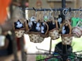 A group of small, realistic-looking black and white toy kittens are nestled in woven baskets hanging from a metal display rack. The baskets are intricately crafted with natural materials, and each one has a metal key ring attached to it. The background is blurred, suggesting an outdoor market setting.