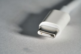 A close-up view of a USB-C connector laying on a smooth surface with soft lighting, highlighting the metallic part of the connector.