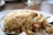 A close-up view of a plate of fried rice featuring a variety of ingredients including chopped vegetables, pieces of seafood, and a mix of herbs and spices. The rice appears golden brown with visible chunks of carrots, onions, and parts of seafood such as octopus tentacles.