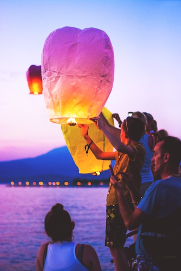 A lively group of friends enjoying a sunset beach party in Thailand, with colorful lanterns glowing overhead.