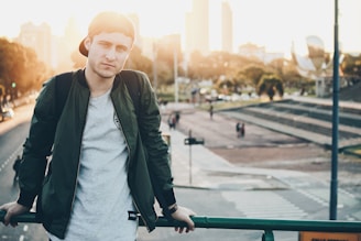 A young adult wearing a sleek, minimalist youly jacket against a city backdrop at sunset.