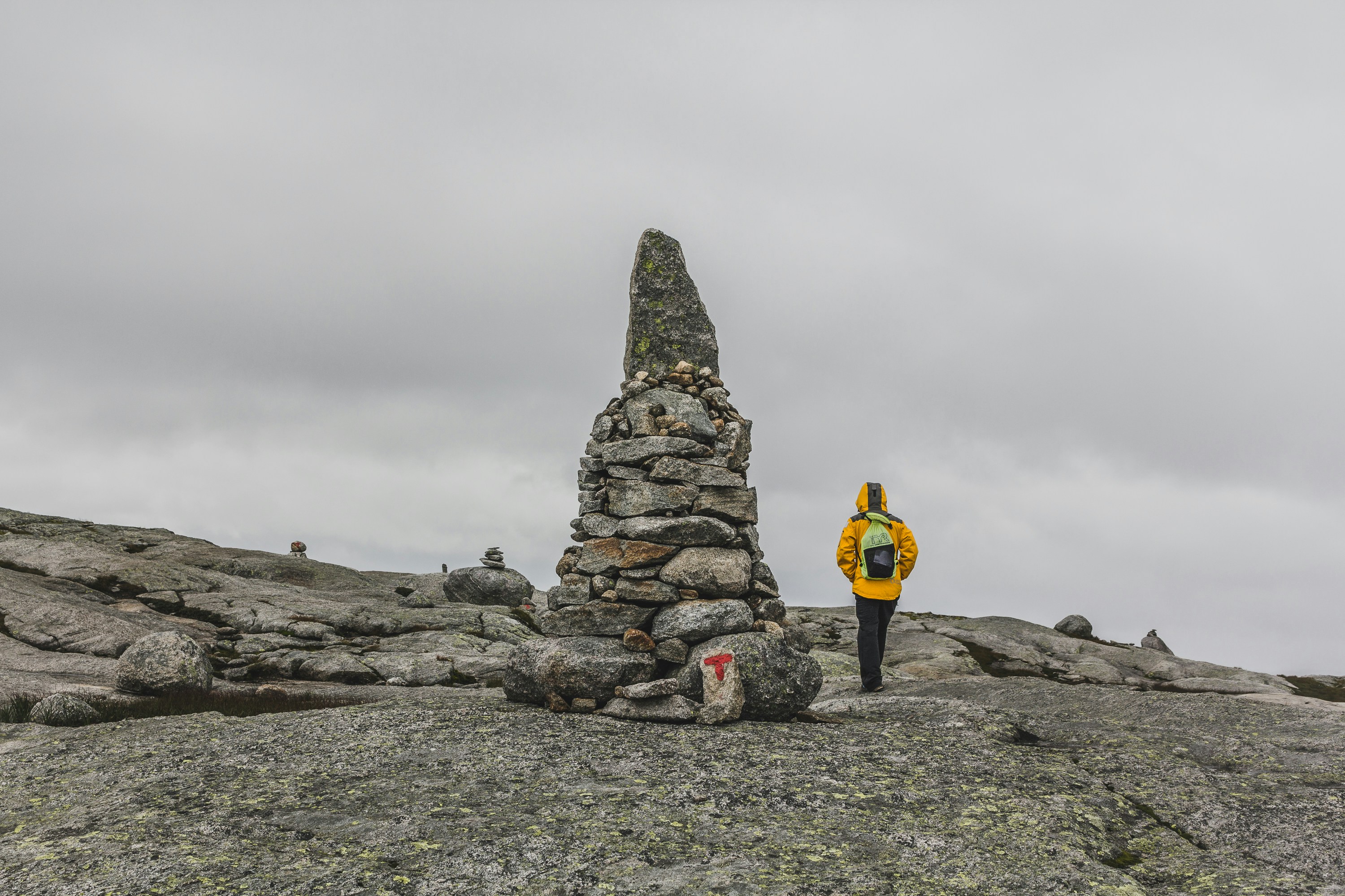 man walking beside rock formation under gray sky