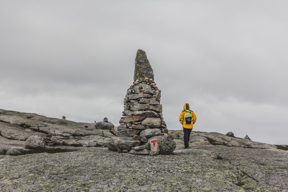 man walking beside rock formation under gray sky