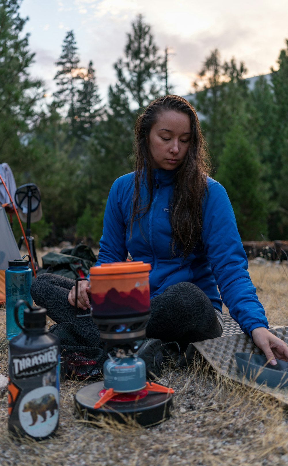 woman sitting on ground with camping stove and mat