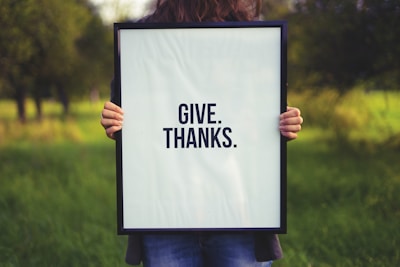 person holding rectangular black wooden photo frame with Give. Thanks. print