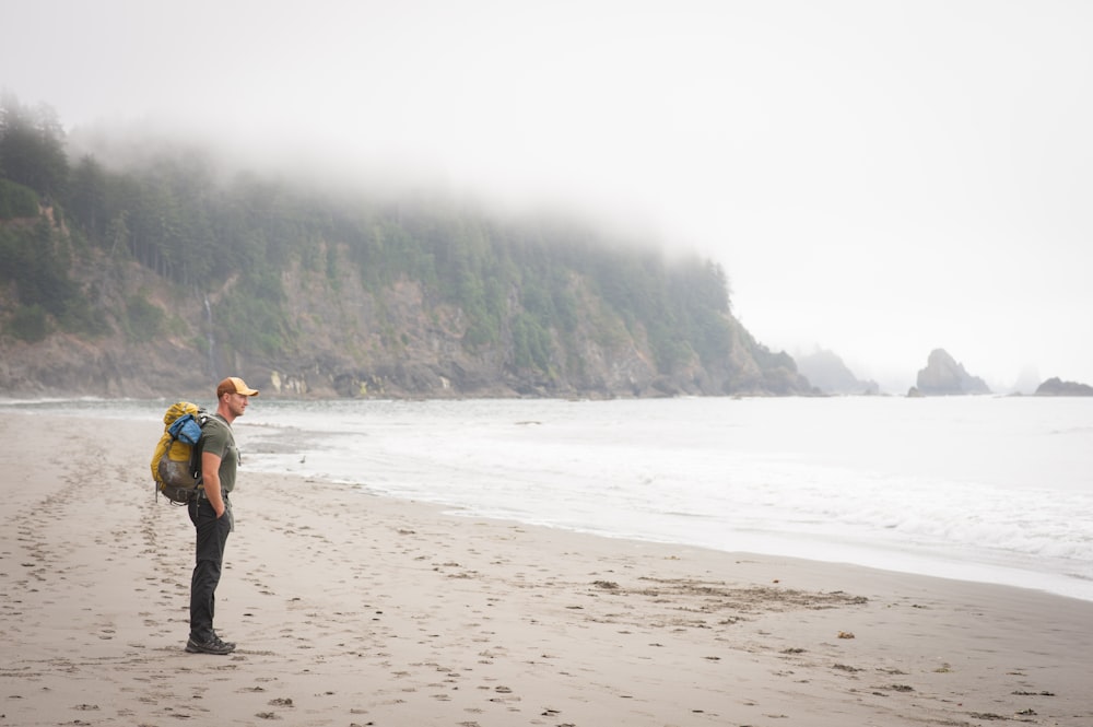 person carrying backpack standing on sea shore