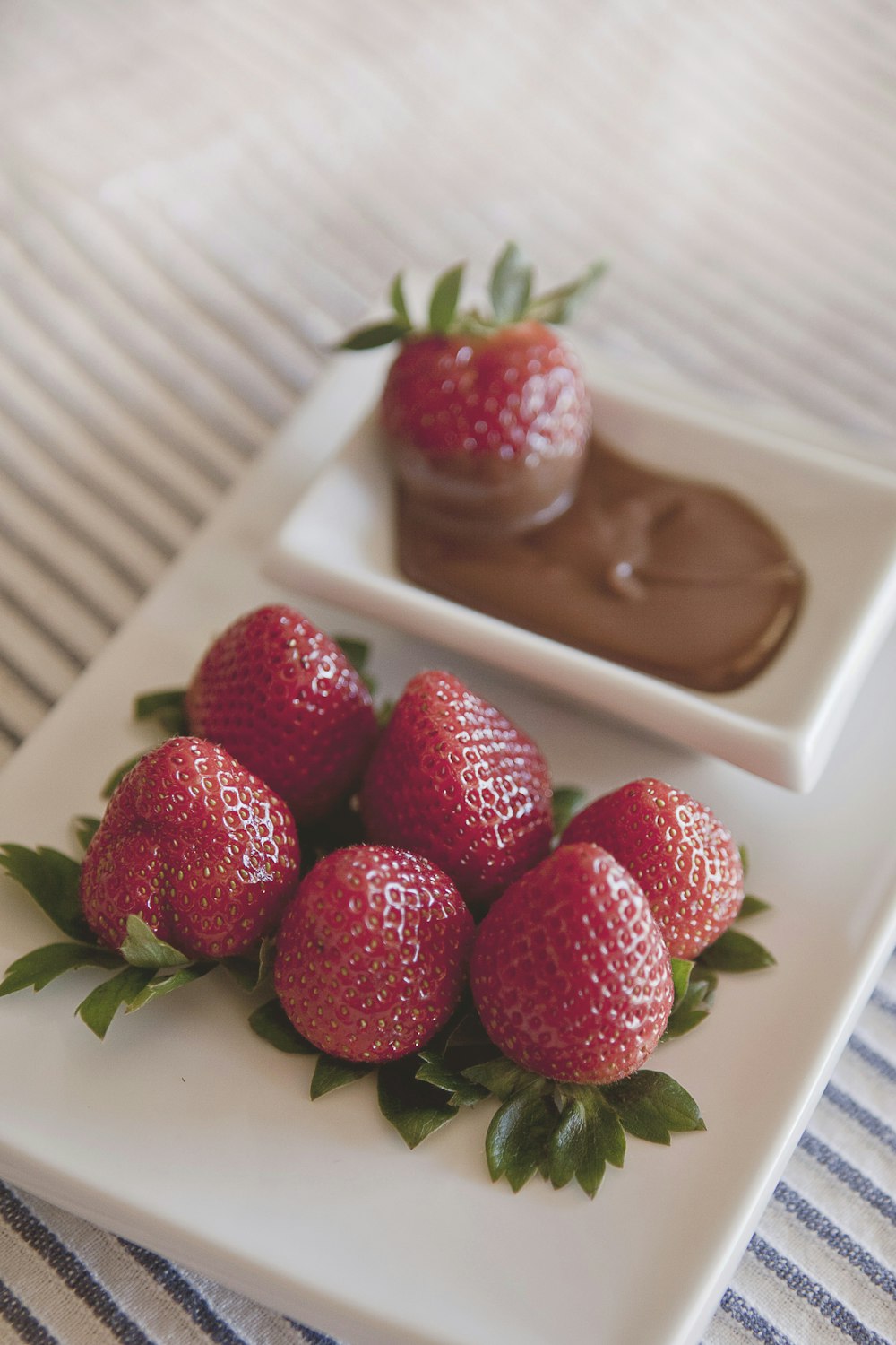 platter of strawberries with chocolate dip on on white surface