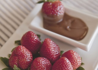 platter of strawberries with chocolate dip on on white surface
