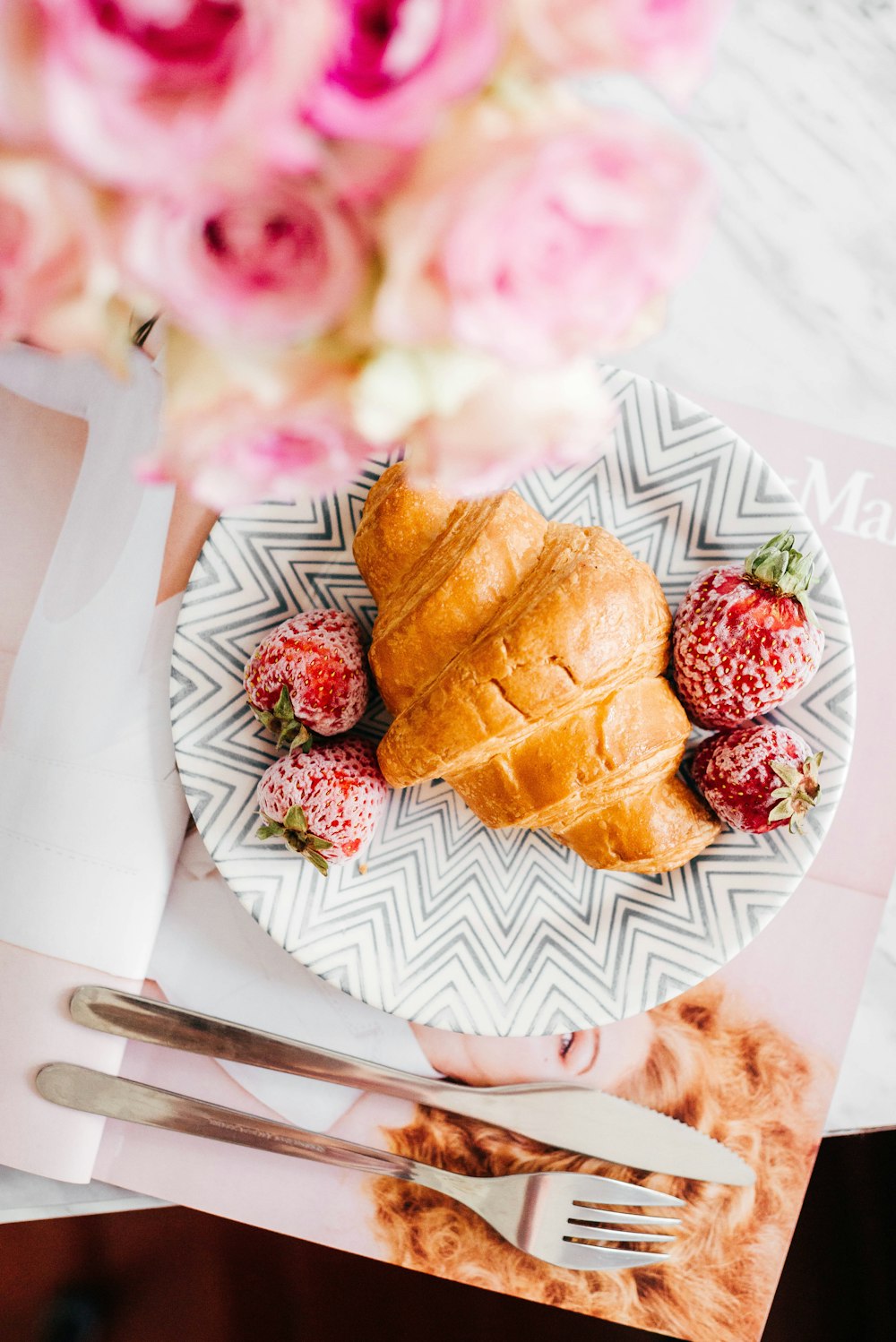 croissant bread and stawberries on beside fork and knife