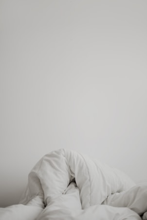 A crumpled white comforter or blanket is partially unfolded against a plain, light-colored background.