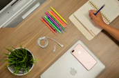 Close-up of hands organizing a planner and digital devices on a clean desk.