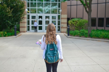 A student with a backpack and books standing in front of a university building.