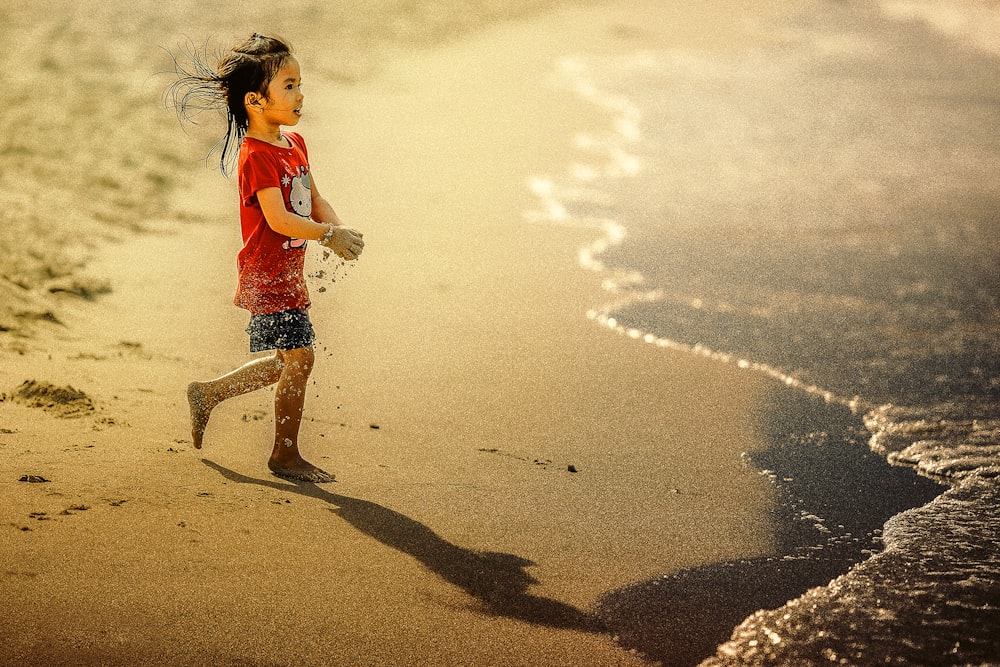 Mädchen trägt Sand auf den Händen, während sie in Richtung Gewässer geht