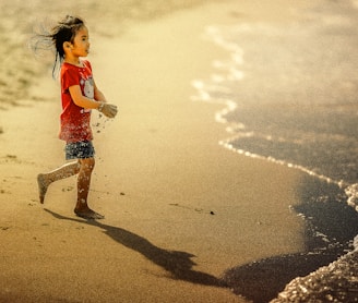 girl carrying sand on her hands while walking towards body of water