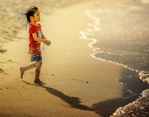 girl carrying sand on her hands while walking towards body of water