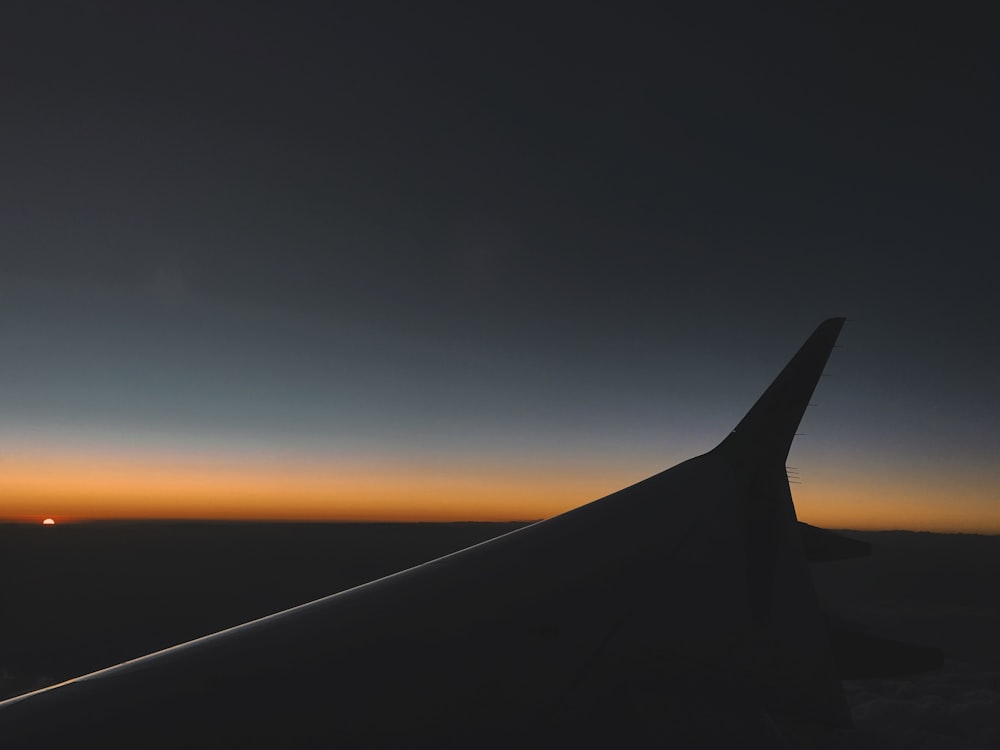 Silhouette of an airplane wing against a blue and yellow sunset