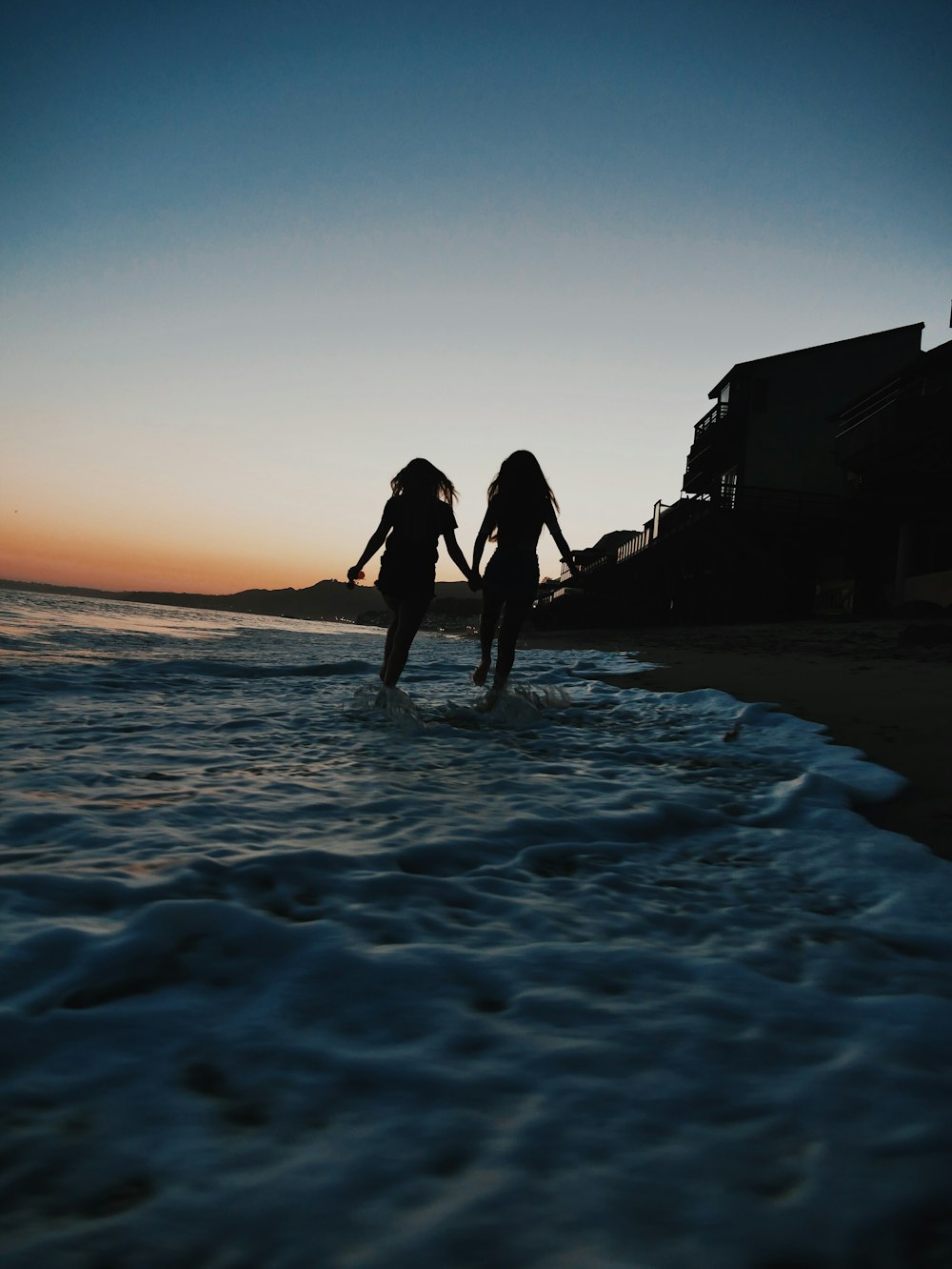 silhouette of two women running across seashore