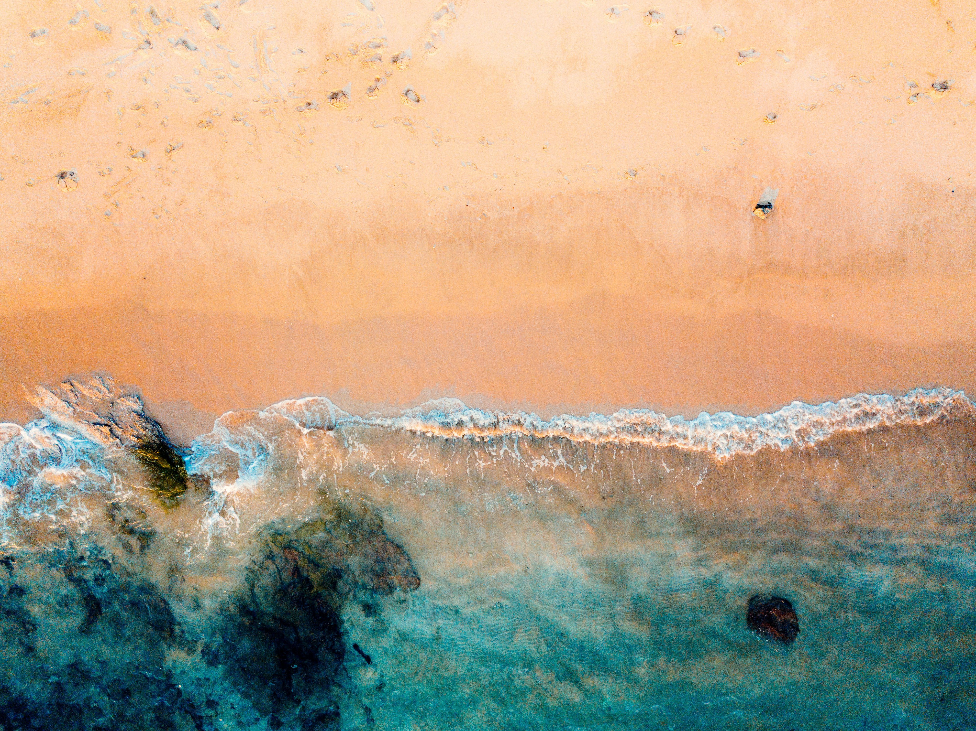 drone shot of beach and body of water on brown sand