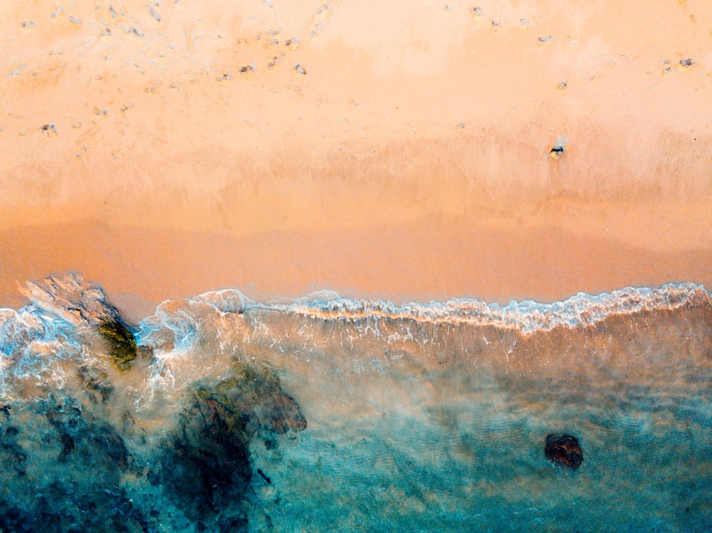 drone shot of beach and body of water on brown sand