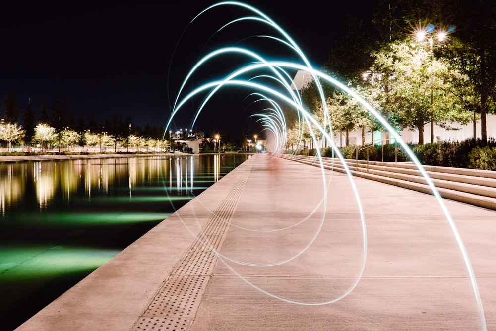 gray pavement beside body of water at night time